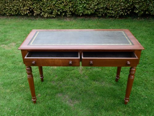 fig 6. A Victorian warm brown mahogany writing table featuring an inset green leather writing surface, two drawers with knob handles, and turned legs.