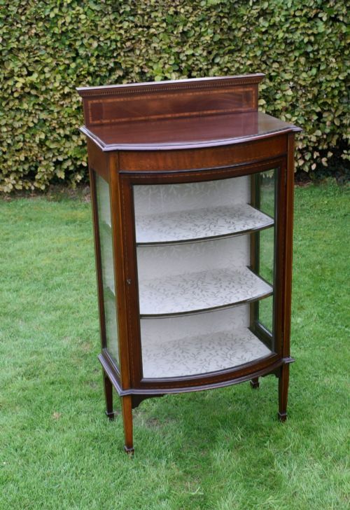 fig 1. An Edwardian mahogany bowfront display cabinet featuring curved glass doors, satinwood string inlay, lined interior shelves, and tapered square legs.