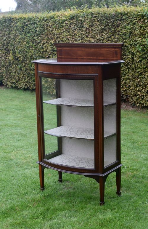 fig 3. An Edwardian mahogany bowfront display cabinet featuring curved glass doors, satinwood string inlay, lined interior shelves, and tapered square legs.