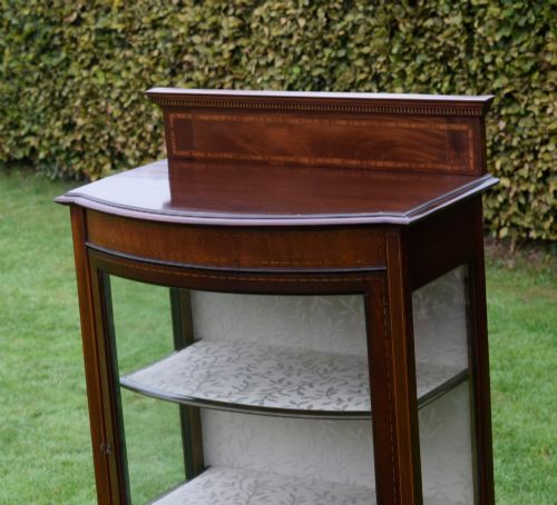 fig 4. An Edwardian mahogany bowfront display cabinet featuring curved glass doors, satinwood string inlay, lined interior shelves, and tapered square legs.