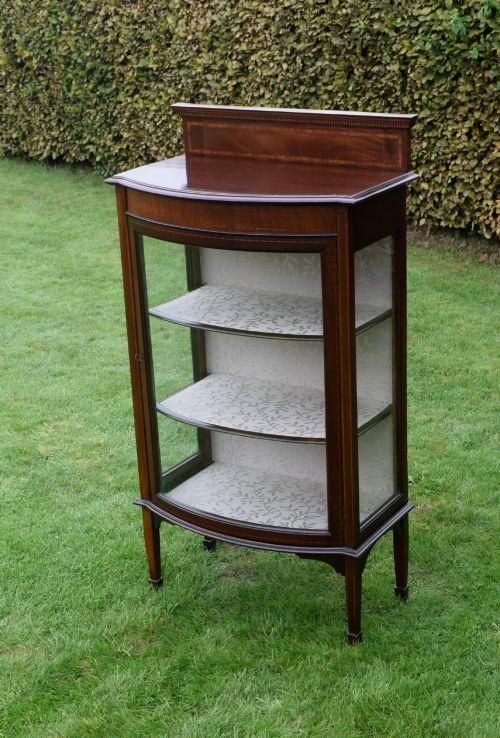 fig 5. An Edwardian mahogany bowfront display cabinet featuring curved glass doors, satinwood string inlay, lined interior shelves, and tapered square legs.