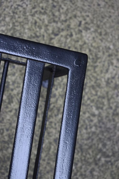 fig 4. A black wrought iron fireplace footman featuring a slatted top with a central decorative cutout handle, resting on four curved legs with flat circular feet.