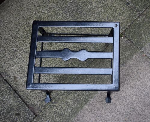 fig 5. A black wrought iron fireplace footman featuring a slatted top with a central decorative cutout handle, resting on four curved legs with flat circular feet.