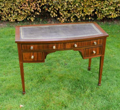 fig 1. An Edwardian inlaid mahogany writing desk featuring a green leather inset top with gold tooling, four drawers with brass handles, and square tapered legs.
