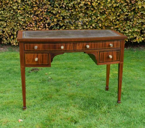 fig 2. An Edwardian inlaid mahogany writing desk featuring a green leather inset top with gold tooling, four drawers with brass handles, and square tapered legs.