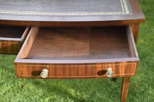 fig 7. An Edwardian inlaid mahogany writing desk featuring a green leather inset top with gold tooling, four drawers with brass handles, and square tapered legs.