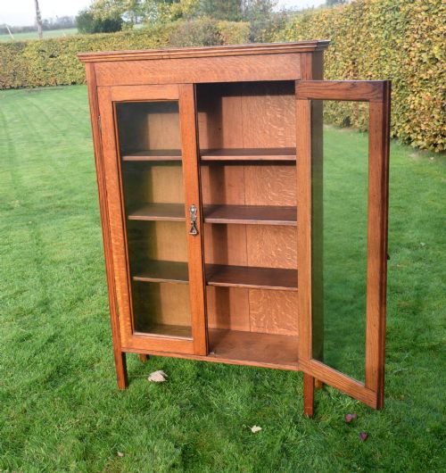 fig 4. An early twentieth-century warm brown oak bookcase featuring twin glazed doors, brass hardware, and three internal shelves.