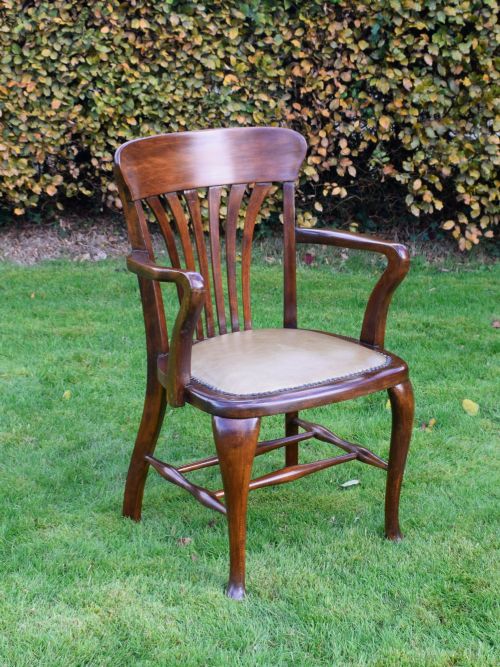 fig 2. A late Victorian wooden desk armchair with a curved slatted backrest, curved arms, and a tan leather seat trimmed with studding.