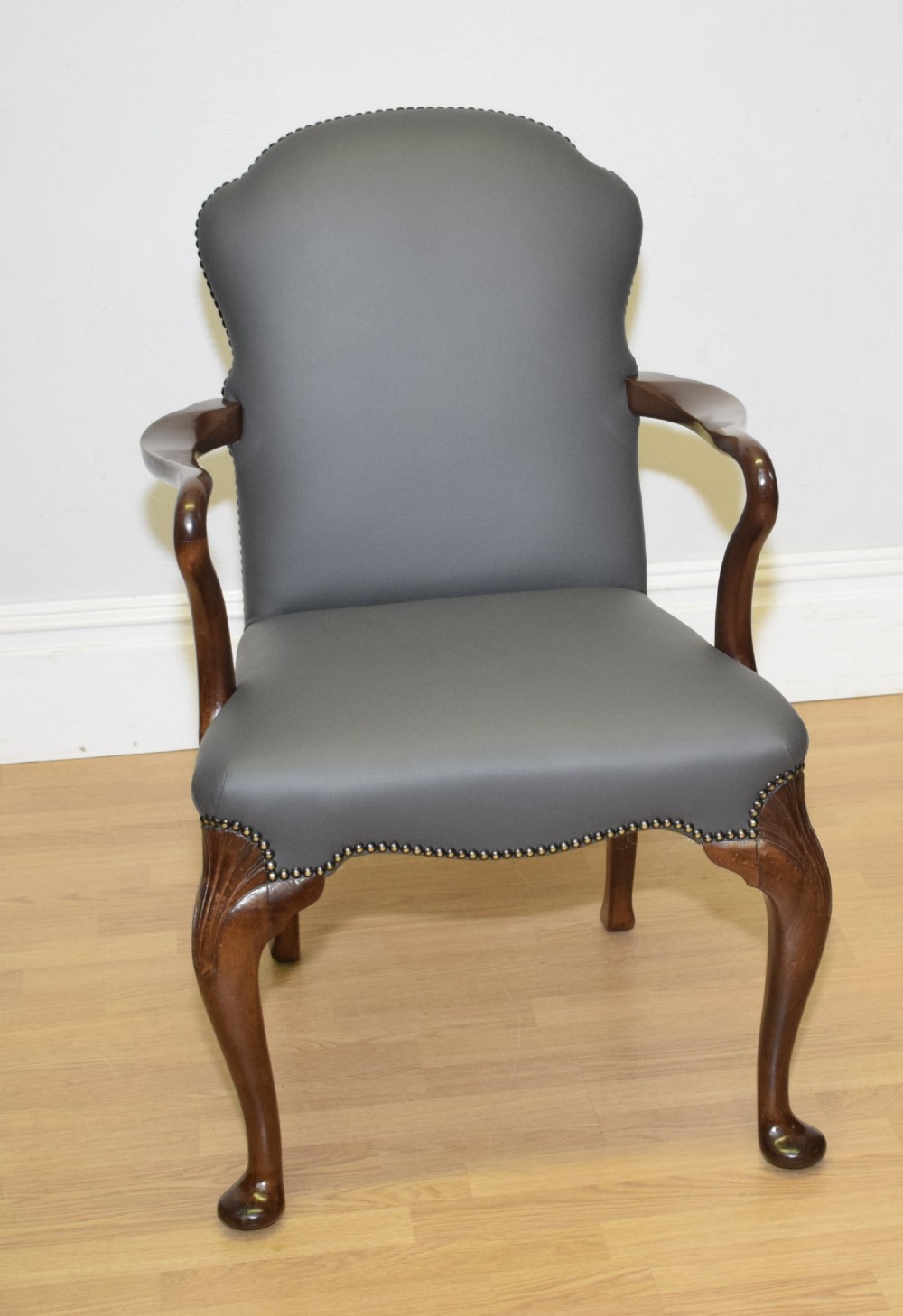 A Queen Anne style grey leather upholstered desk chair featuring carved mahogany cabriole legs, brass studding detail, and sweeping arms.