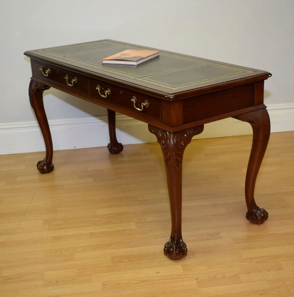 A mahogany library writing table featuring a green leather inset top, brass drop handles, and carved cabriole legs terminating in claw and ball feet.