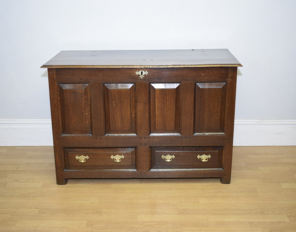 A dark Georgian oak mule chest featuring four fielded front panels and two lower drawers with brass swan-neck handles.