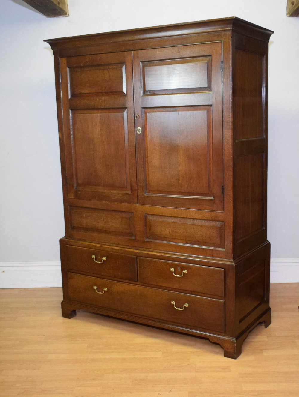 A two-piece Georgian oak press cupboard featuring twin fielded panel doors over a three-drawer base with brass handles. View II