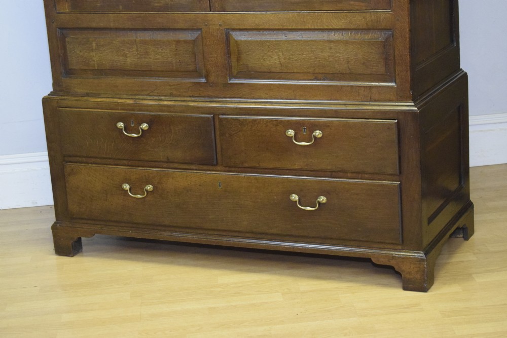 A two-piece Georgian oak press cupboard featuring twin fielded panel doors over a three-drawer base with brass handles. View V