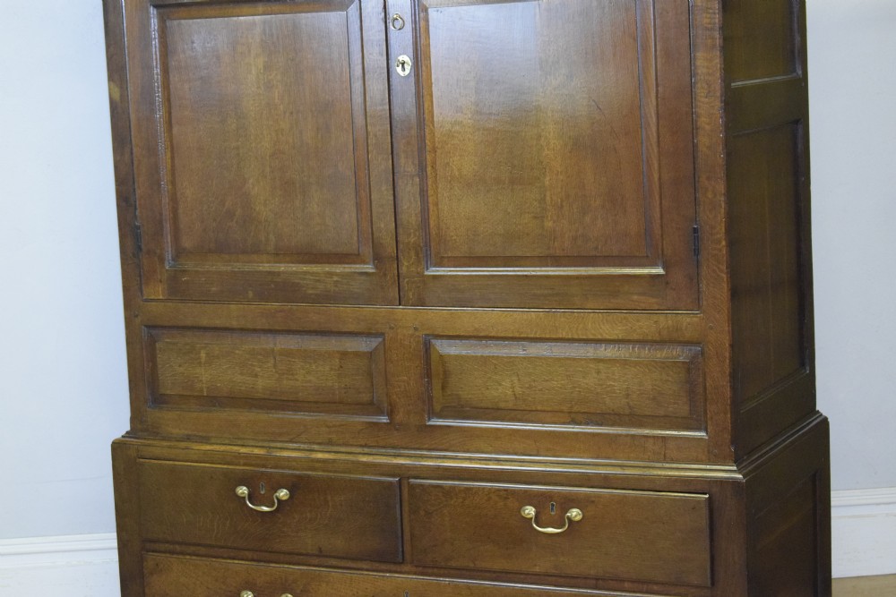 A two-piece Georgian oak press cupboard featuring twin fielded panel doors over a three-drawer base with brass handles. View VI