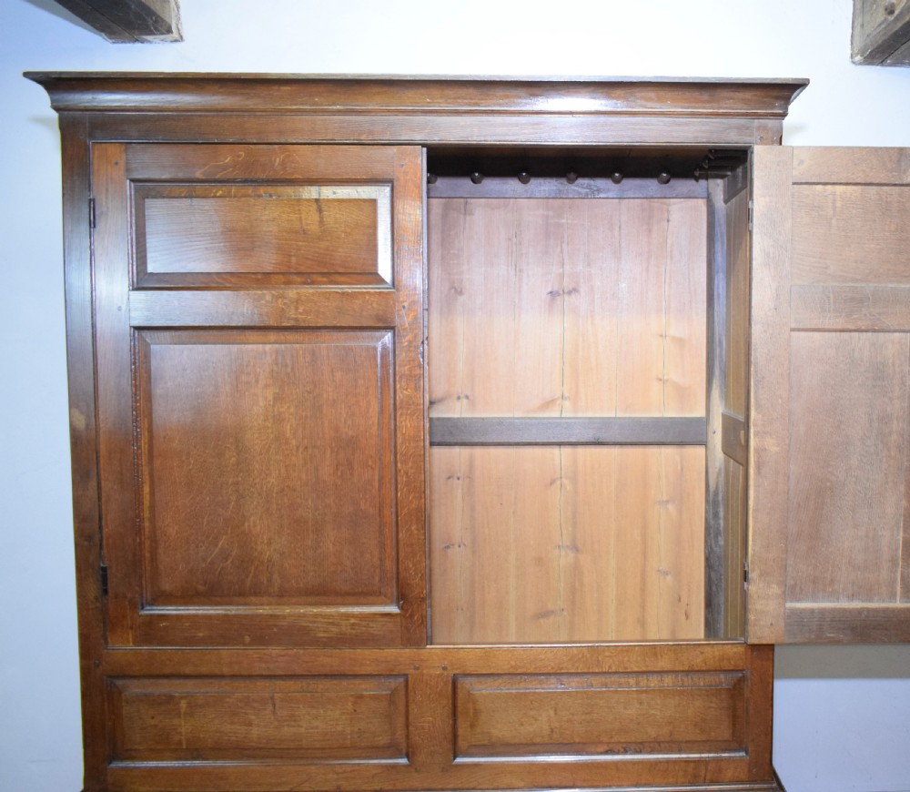 A two-piece Georgian oak press cupboard featuring twin fielded panel doors over a three-drawer base with brass handles. View XV