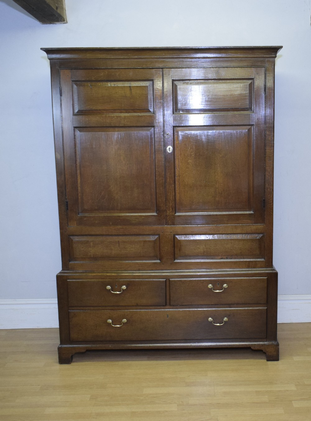 A two-piece Georgian oak press cupboard featuring twin fielded panel doors over a three-drawer base with brass handles. View XVI