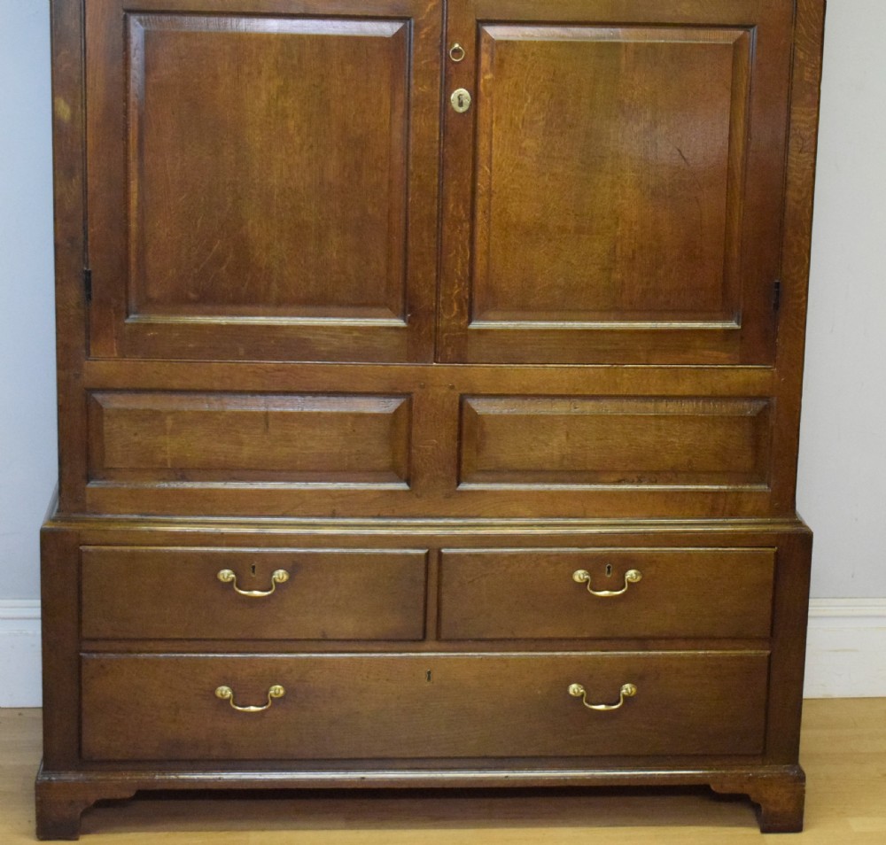 A two-piece Georgian oak press cupboard featuring twin fielded panel doors over a three-drawer base with brass handles. View XVIII