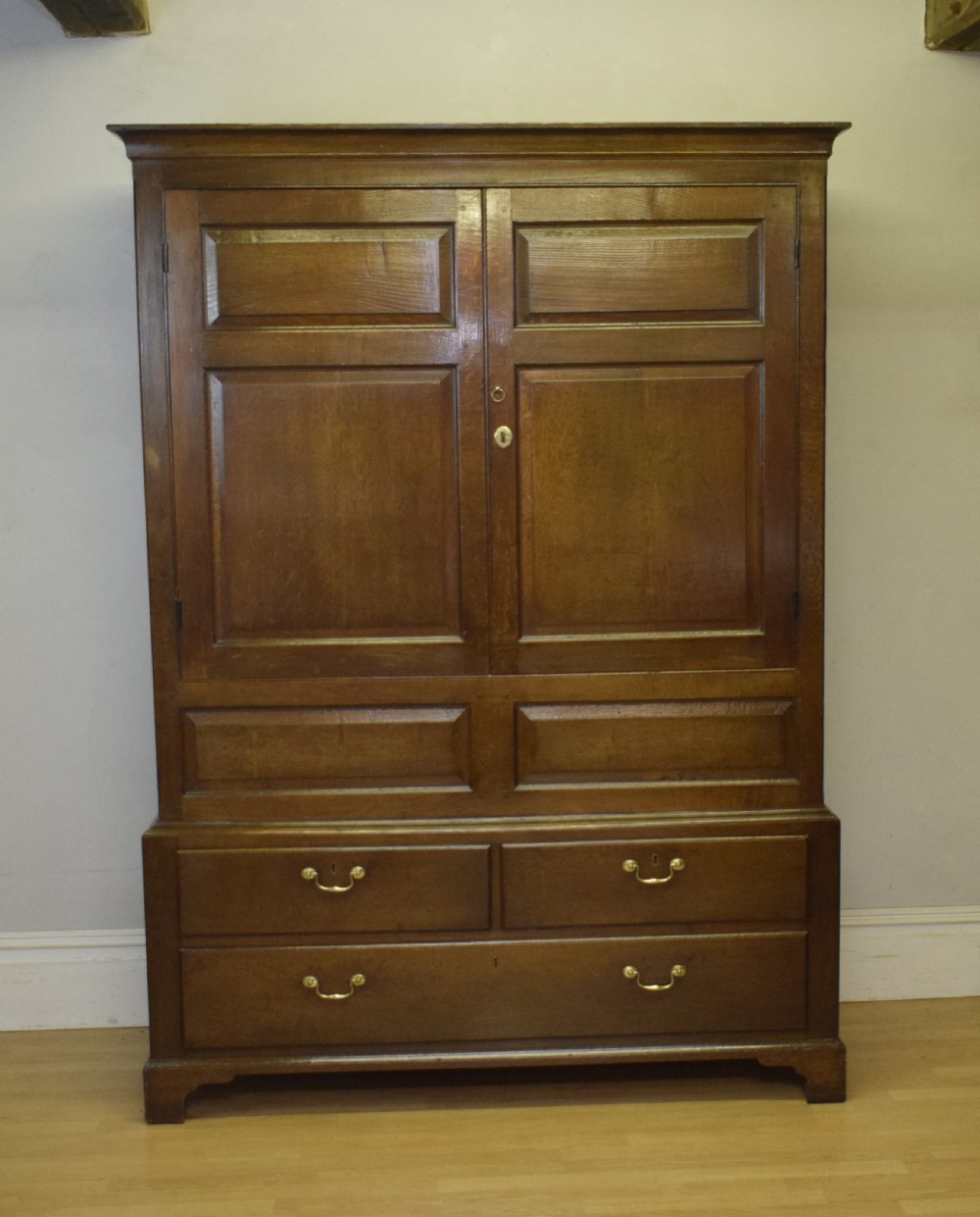 A two-piece Georgian oak press cupboard featuring twin fielded panel doors over a three-drawer base with brass handles. View XX