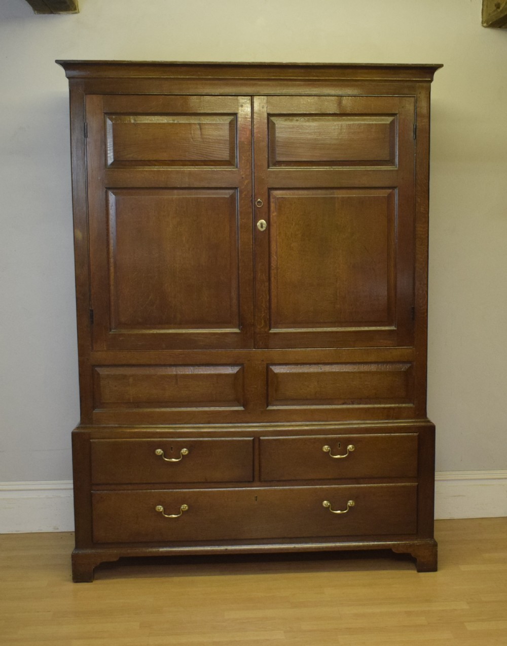 A two-piece Georgian oak press cupboard featuring twin fielded panel doors over a three-drawer base with brass handles. View XXI