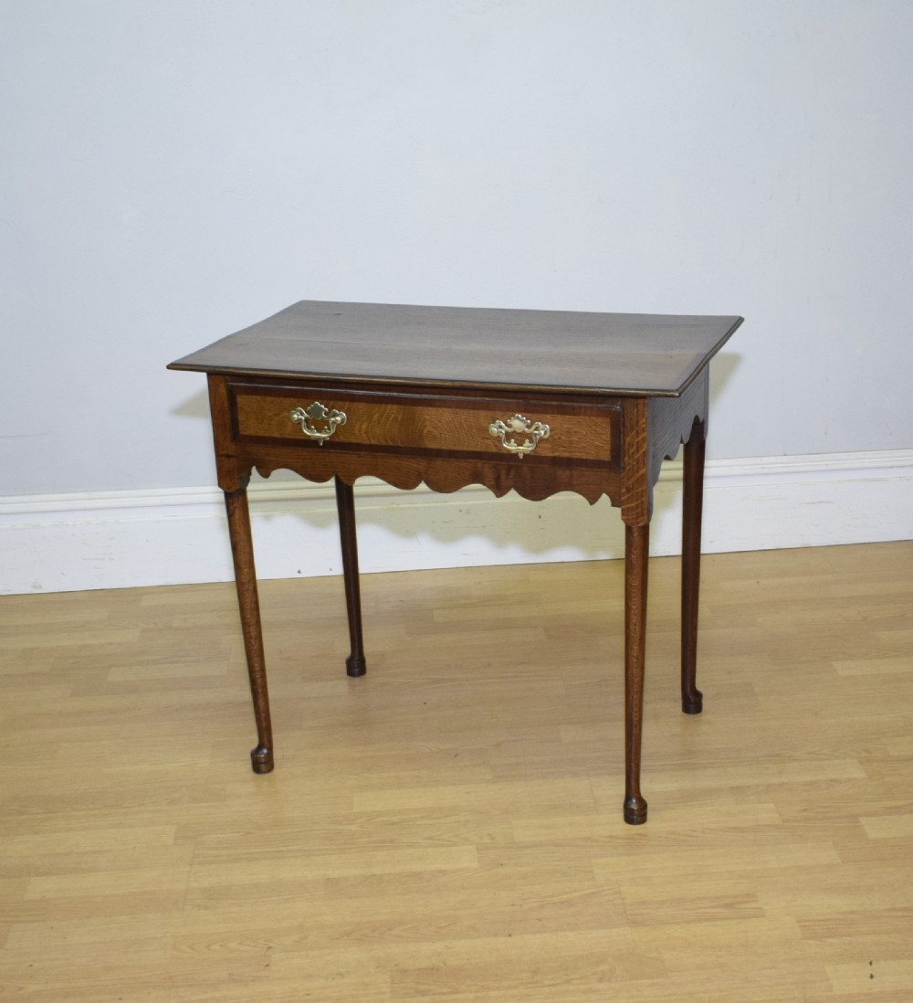 A Georgian oak lowboy side table featuring a single drawer with brass swan-neck handles and a scalloped lower apron.