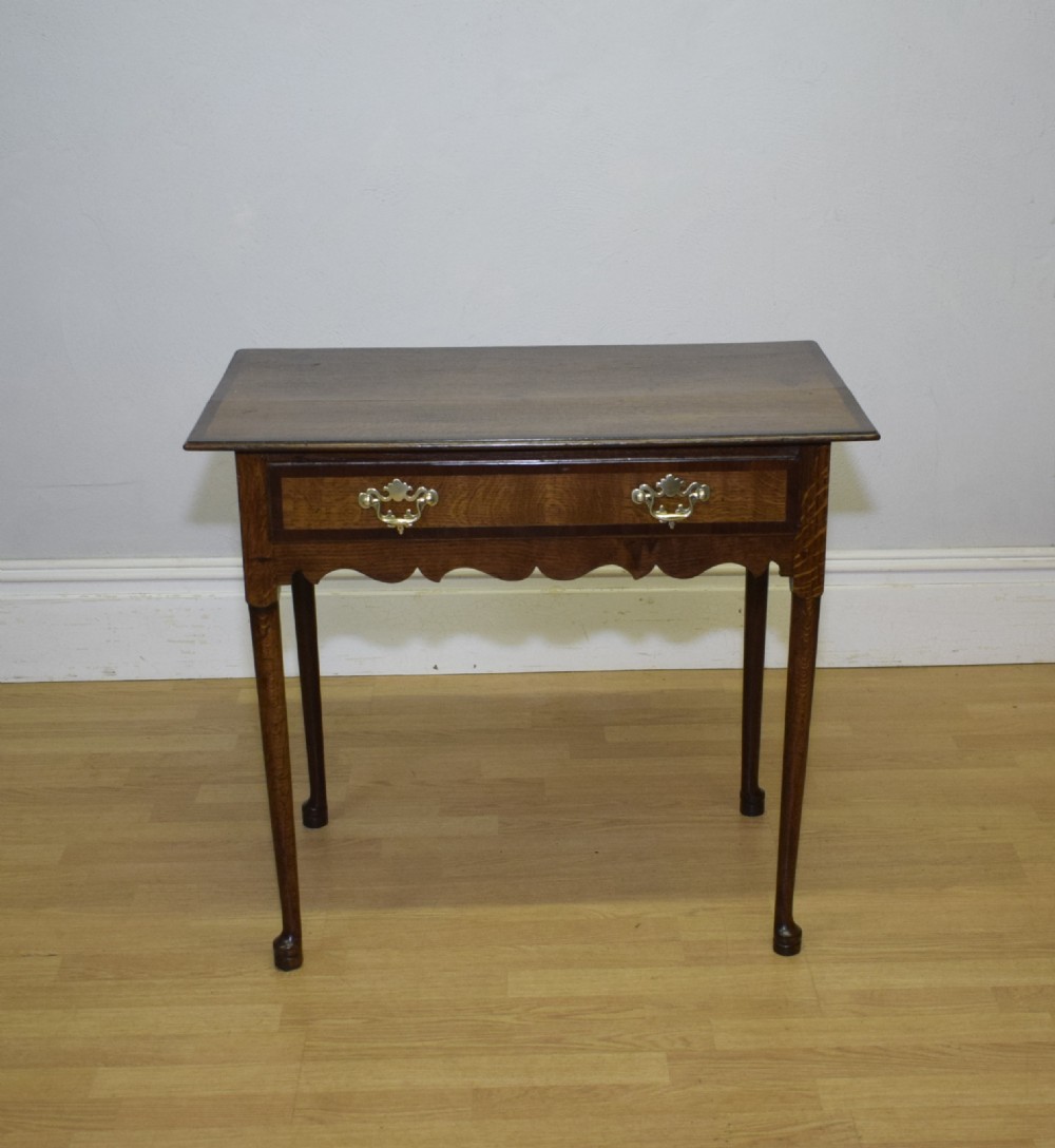 A Georgian oak lowboy side table featuring a single drawer with brass swan-neck handles and a scalloped lower apron. View V