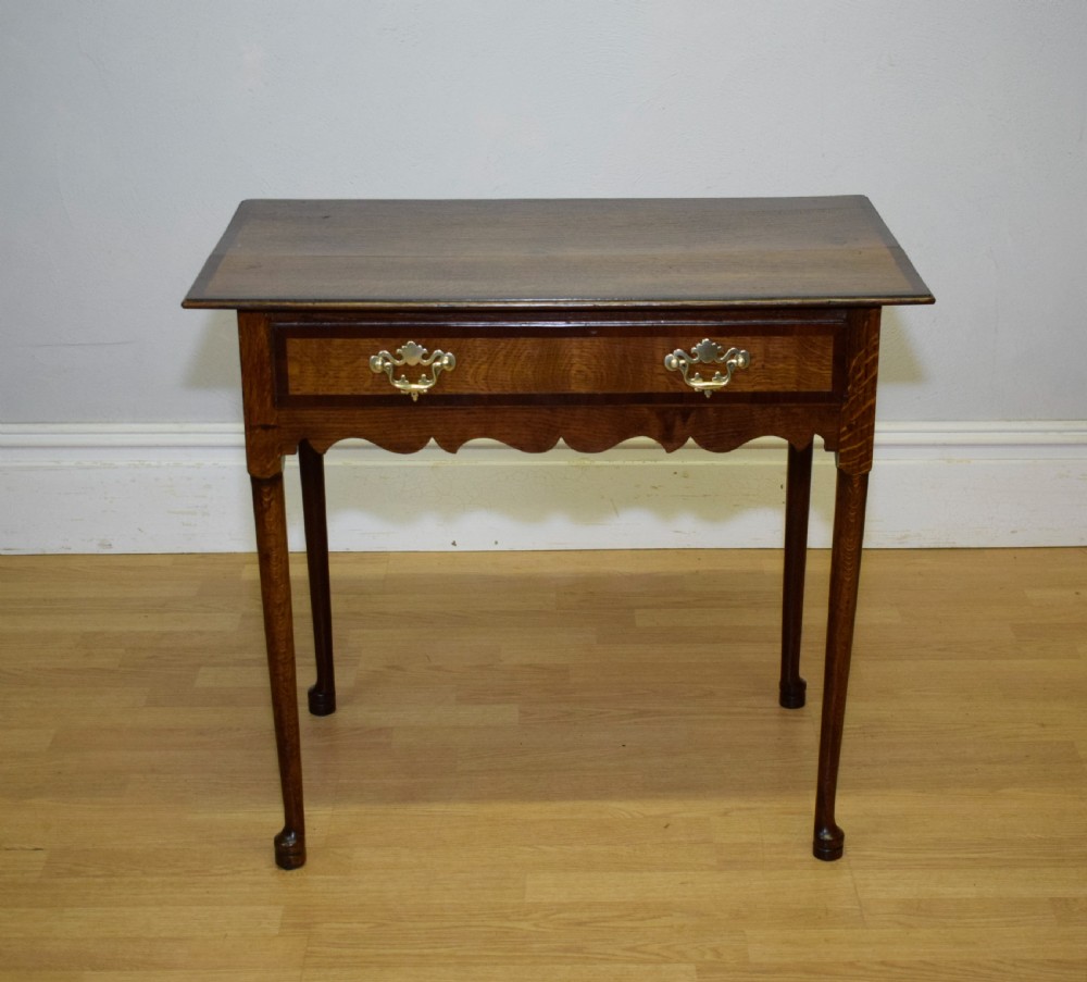 A Georgian oak lowboy side table featuring a single drawer with brass swan-neck handles and a scalloped lower apron. View VI