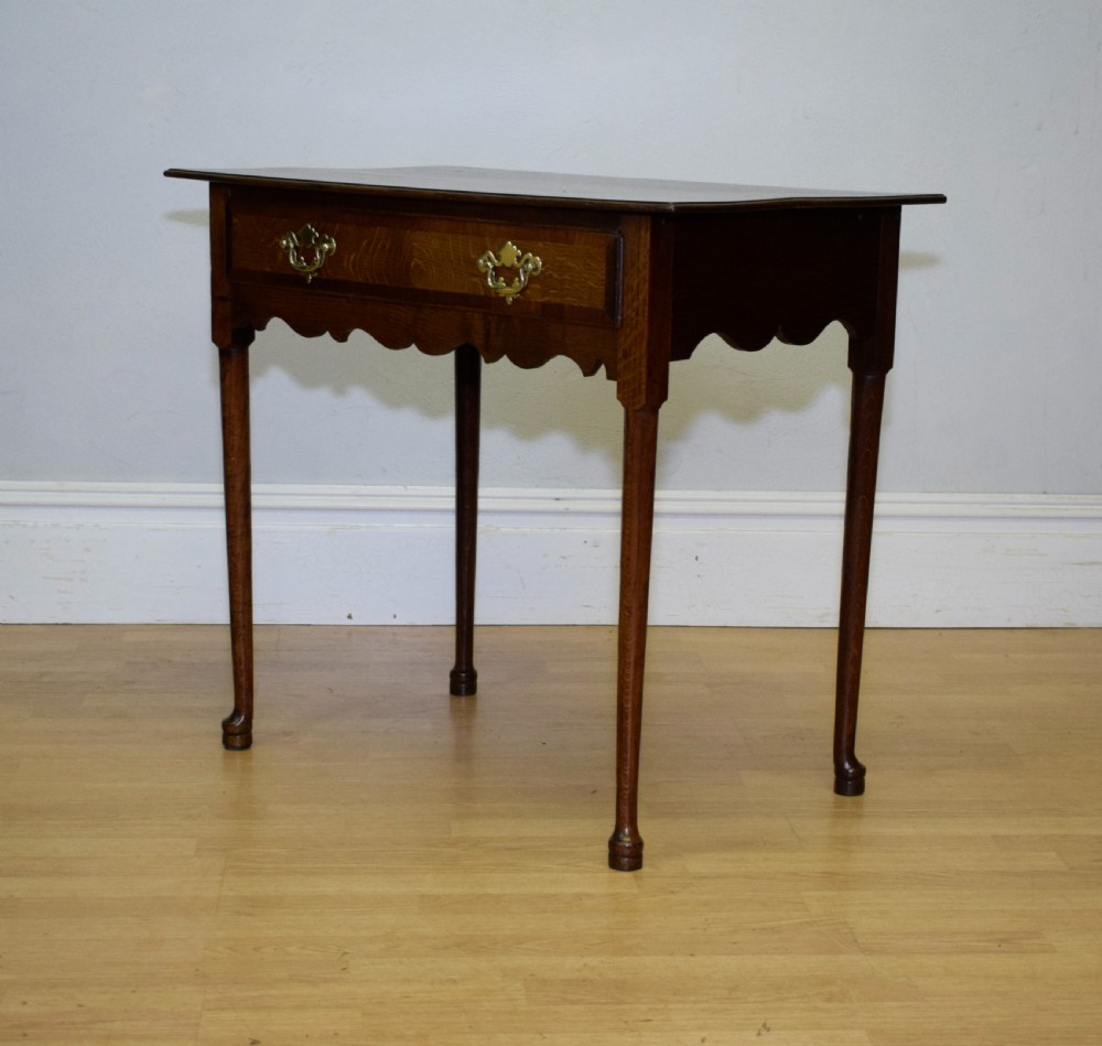 A Georgian oak lowboy side table featuring a single drawer with brass swan-neck handles and a scalloped lower apron. View X