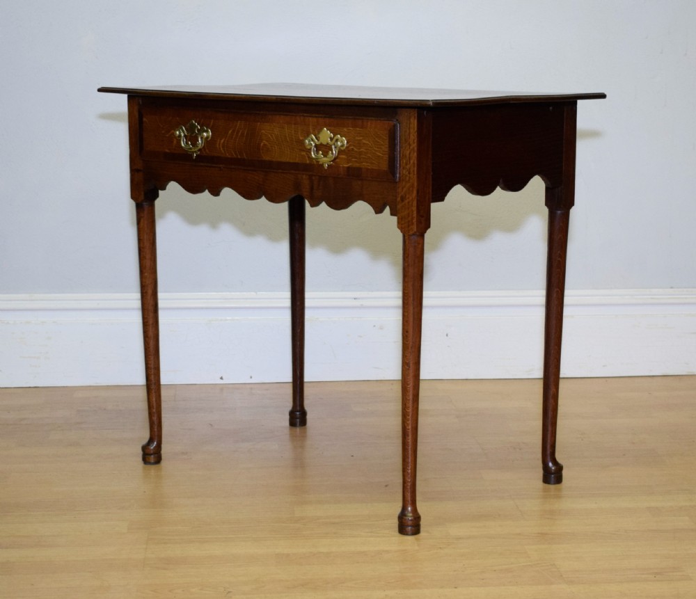A Georgian oak lowboy side table featuring a single drawer with brass swan-neck handles and a scalloped lower apron. View XI