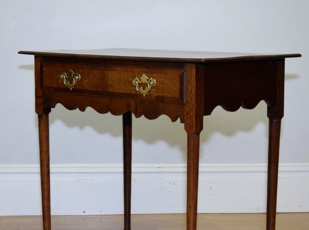 A Georgian oak lowboy side table featuring a single drawer with brass swan-neck handles and a scalloped lower apron. View XII