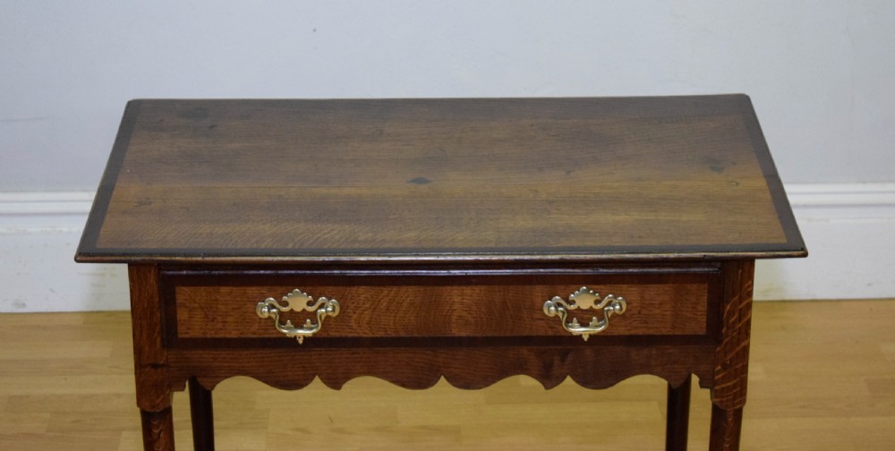 A Georgian oak lowboy side table featuring a single drawer with brass swan-neck handles and a scalloped lower apron. View XV
