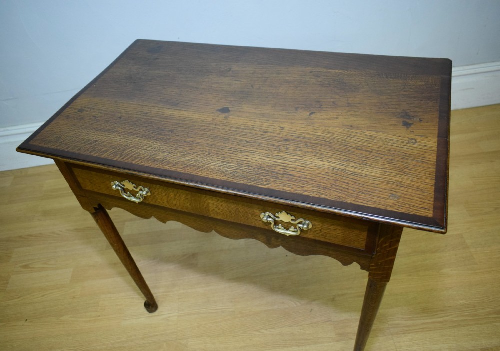 A Georgian oak lowboy side table featuring a single drawer with brass swan-neck handles and a scalloped lower apron. View XVII