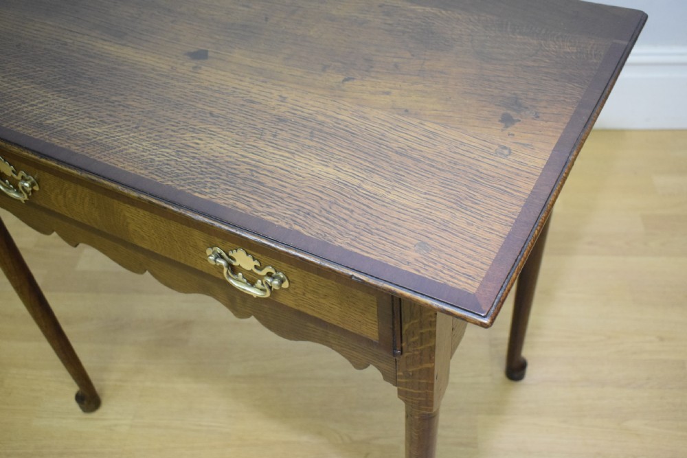 A Georgian oak lowboy side table featuring a single drawer with brass swan-neck handles and a scalloped lower apron. View XVIII