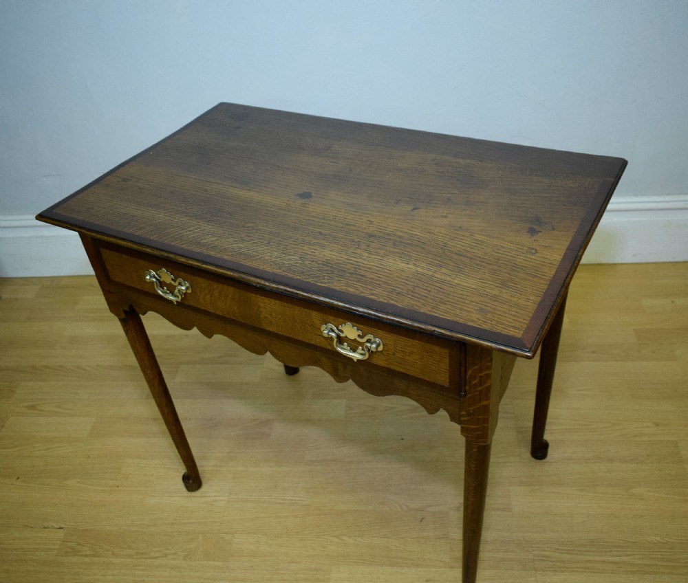 A Georgian oak lowboy side table featuring a single drawer with brass swan-neck handles and a scalloped lower apron. View XIX