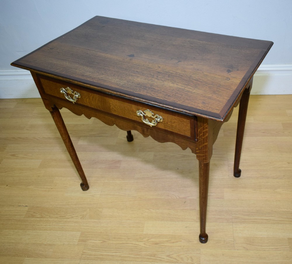 A Georgian oak lowboy side table featuring a single drawer with brass swan-neck handles and a scalloped lower apron. View XX