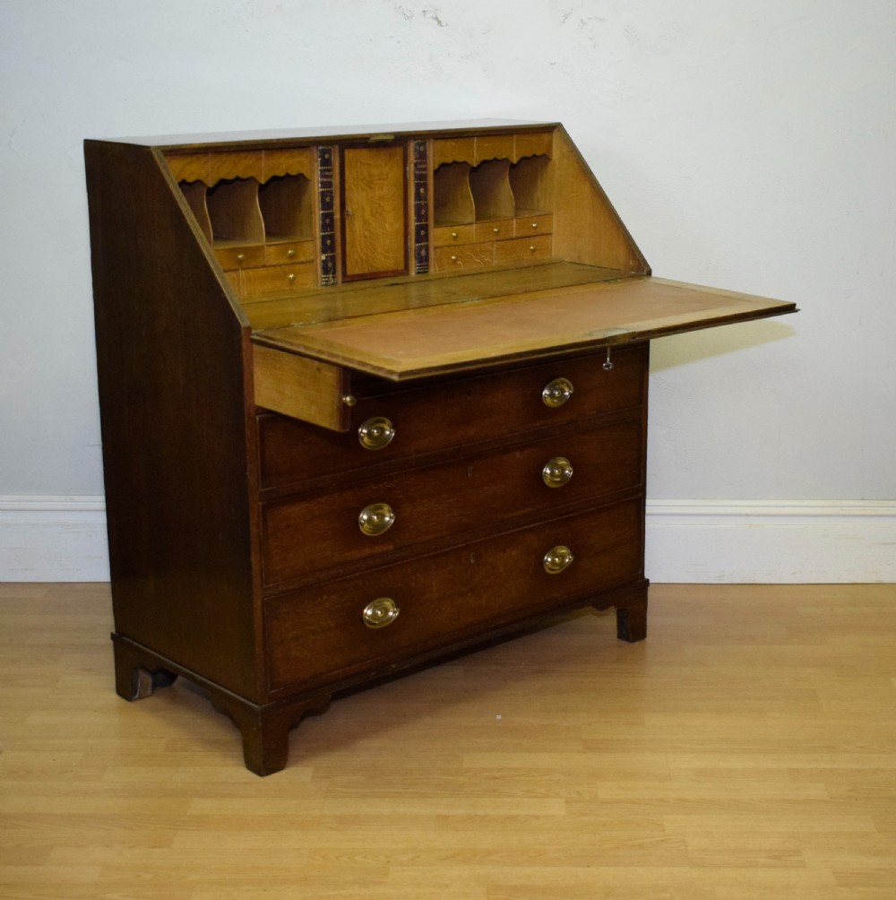 A Georgian oak bureau featuring a slanted fall-front lid above four graduated drawers fitted with brass oval handles and raised on bracket feet. View II