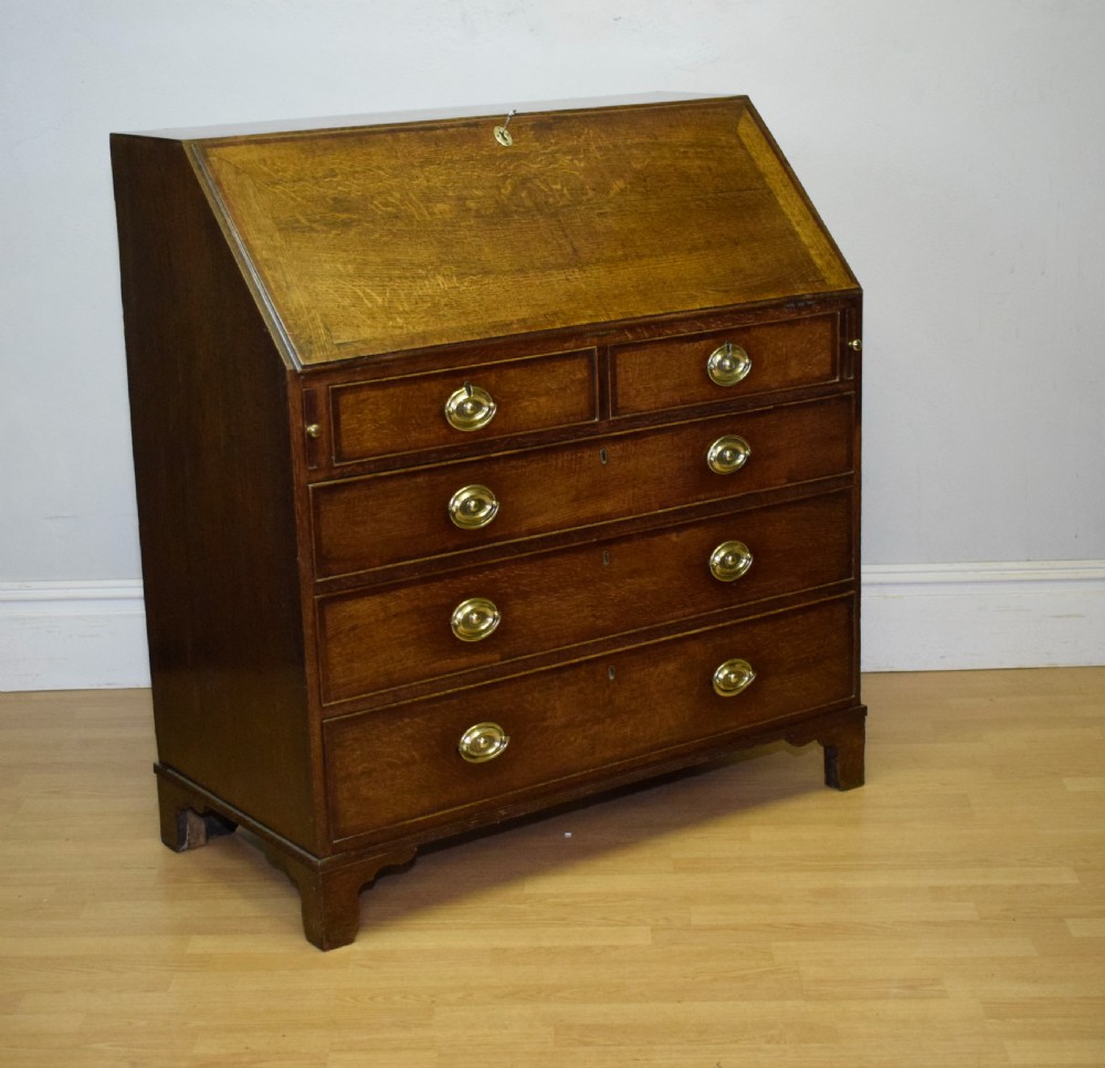 A Georgian oak bureau featuring a slanted fall-front lid above four graduated drawers fitted with brass oval handles and raised on bracket feet. View III