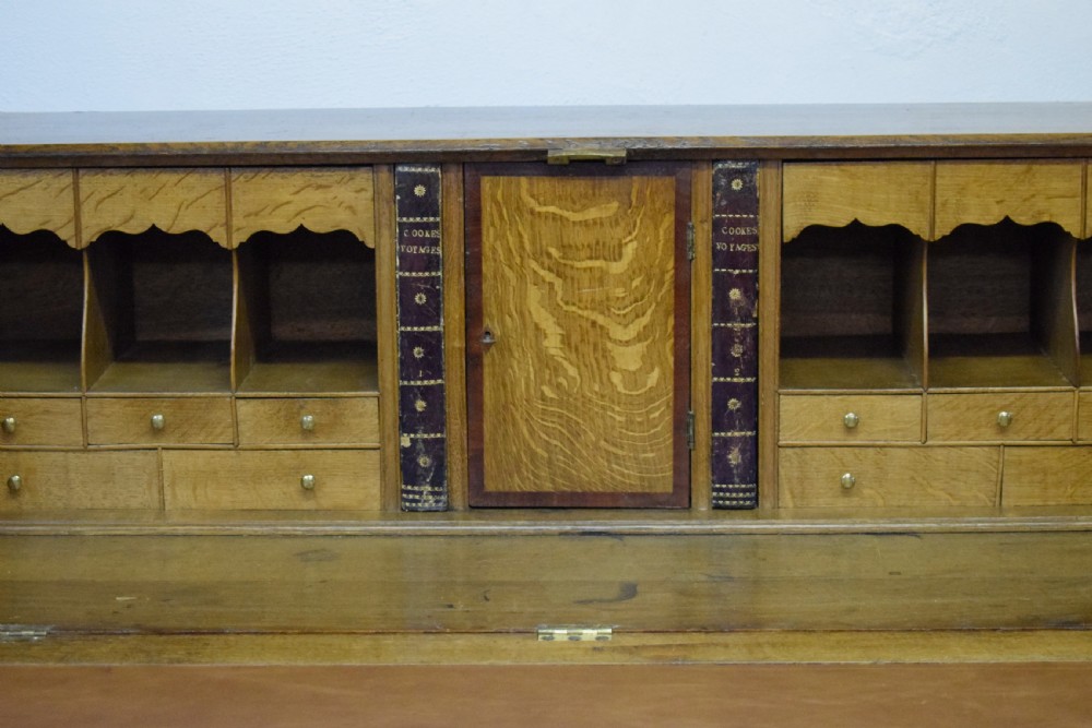 A Georgian oak bureau featuring a slanted fall-front lid above four graduated drawers fitted with brass oval handles and raised on bracket feet. View VI
