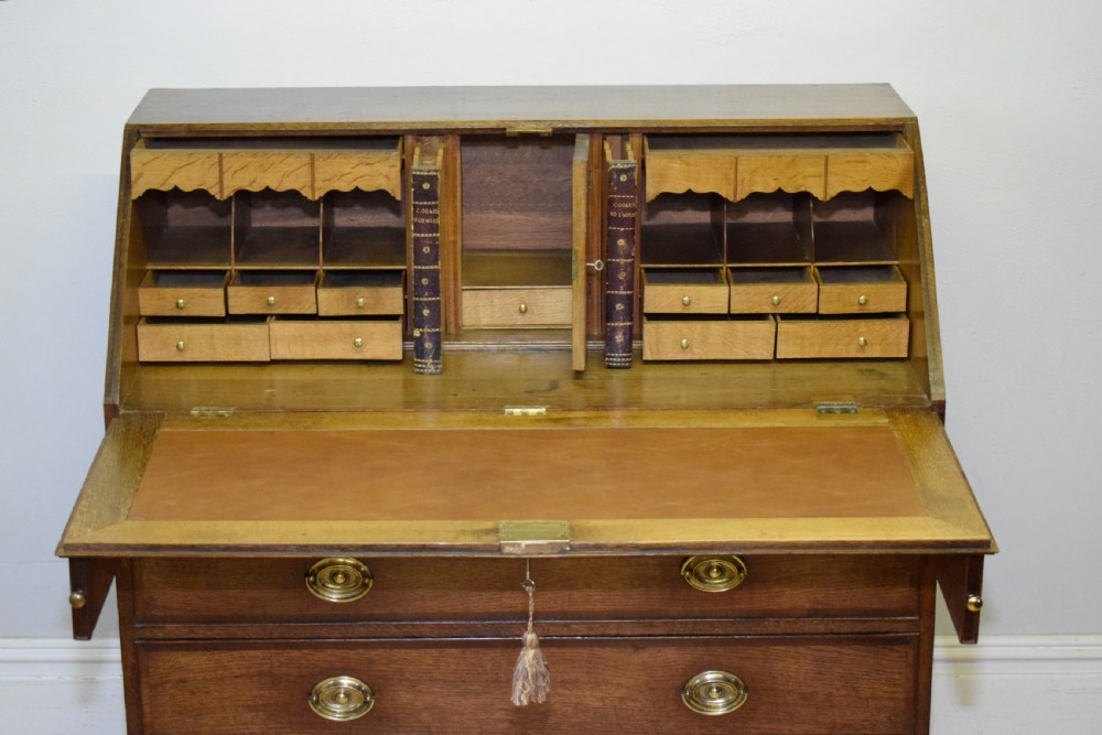 A Georgian oak bureau featuring a slanted fall-front lid above four graduated drawers fitted with brass oval handles and raised on bracket feet. View VIII