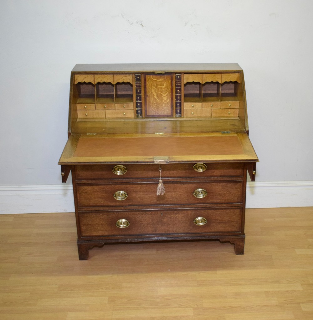 A Georgian oak bureau featuring a slanted fall-front lid above four graduated drawers fitted with brass oval handles and raised on bracket feet. View XIII