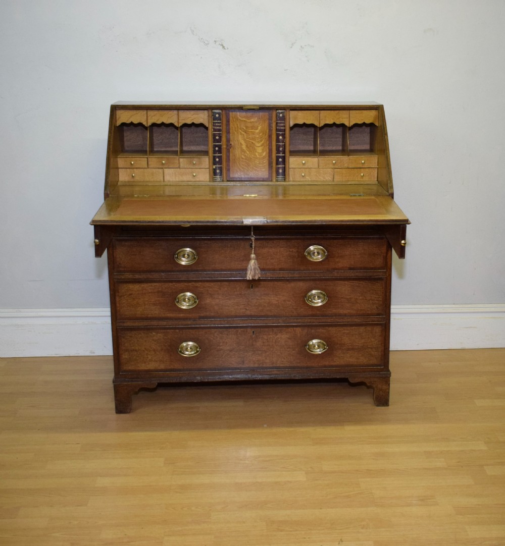 A Georgian oak bureau featuring a slanted fall-front lid above four graduated drawers fitted with brass oval handles and raised on bracket feet. View XIV
