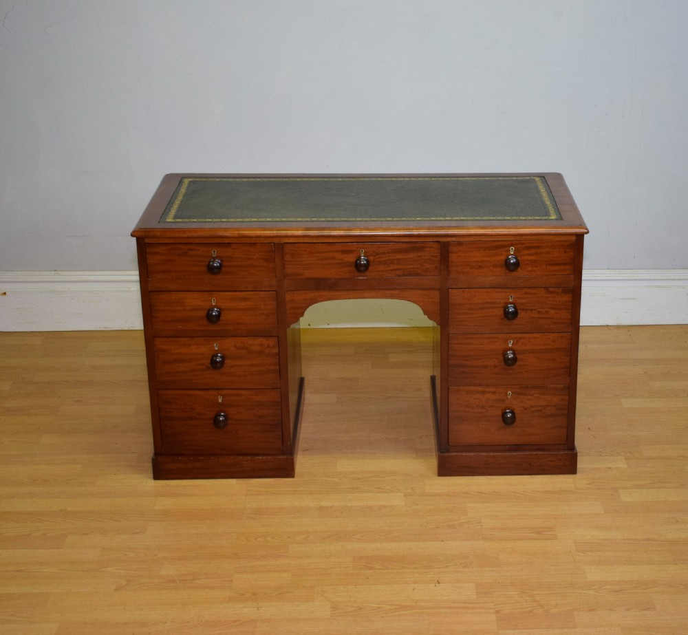 A Victorian mahogany pedestal desk with nine drawers, turned wooden handles, a dark leather insert top, and a central kneehole.