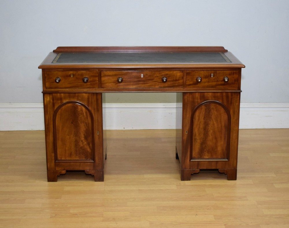 A Victorian mahogany pedestal desk featuring a dark green leather inset writing surface, three frieze drawers, and arched panel pedestal doors. View II