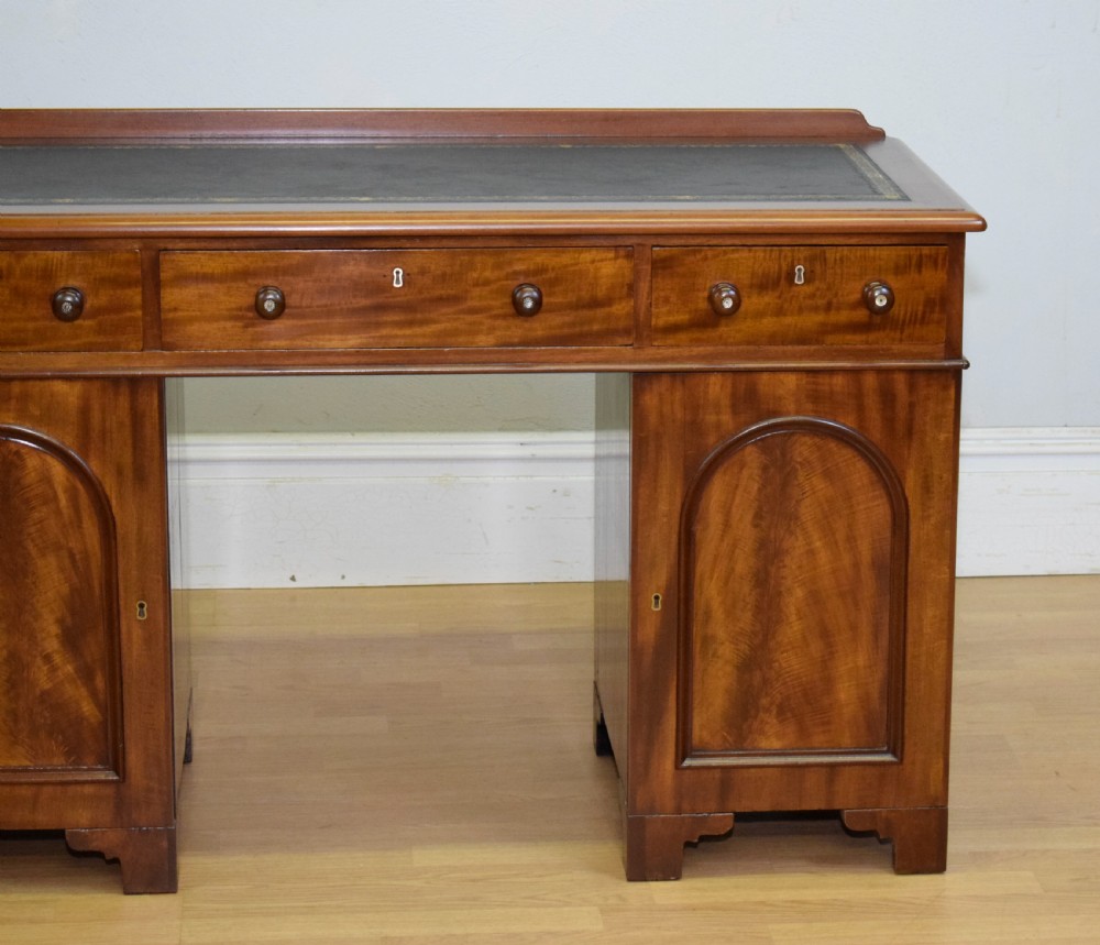 A Victorian mahogany pedestal desk featuring a dark green leather inset writing surface, three frieze drawers, and arched panel pedestal doors. View III