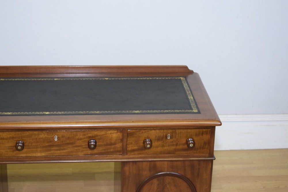 A Victorian mahogany pedestal desk featuring a dark green leather inset writing surface, three frieze drawers, and arched panel pedestal doors. View IX