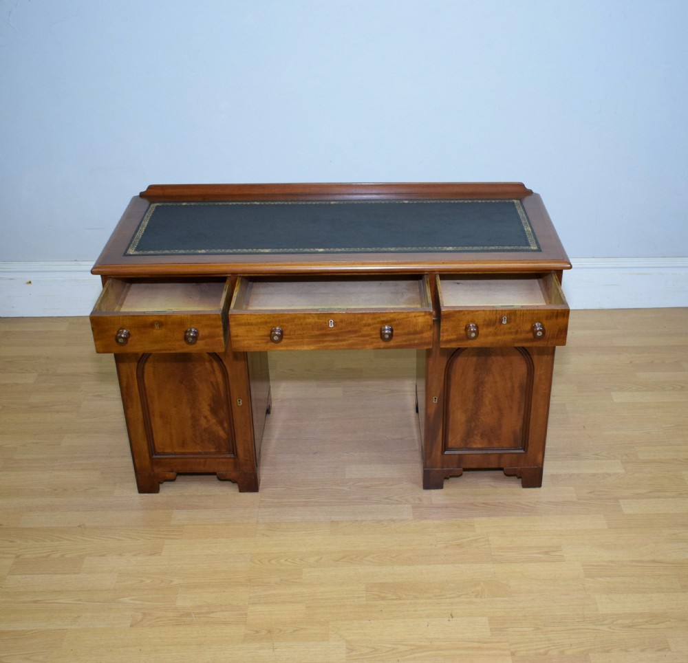 A Victorian mahogany pedestal desk featuring a dark green leather inset writing surface, three frieze drawers, and arched panel pedestal doors. View XI