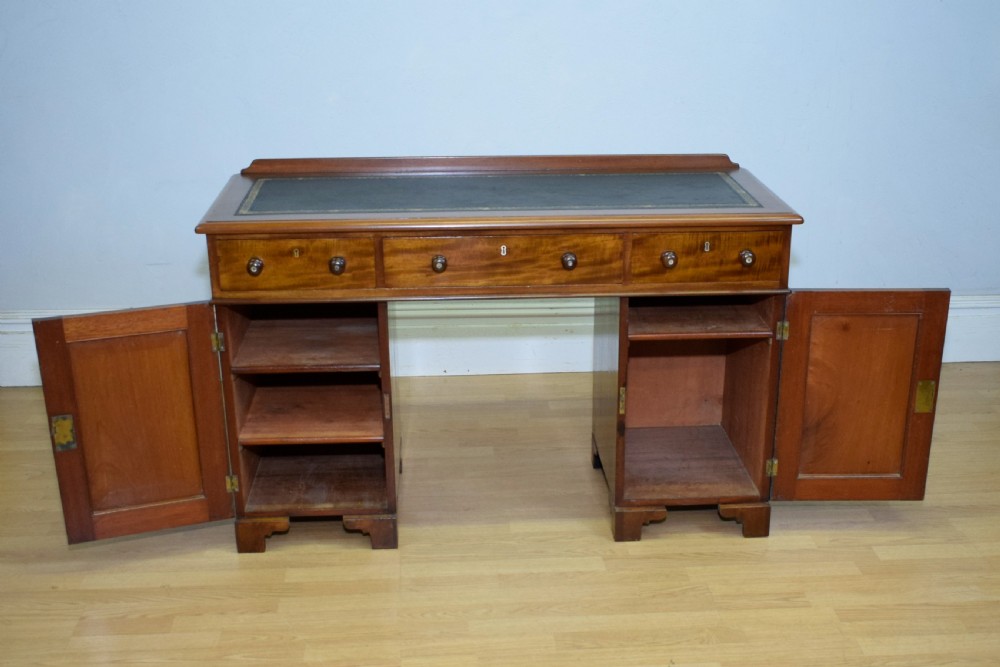 A Victorian mahogany pedestal desk featuring a dark green leather inset writing surface, three frieze drawers, and arched panel pedestal doors. View XII