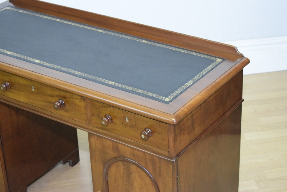 A Victorian mahogany pedestal desk featuring a dark green leather inset writing surface, three frieze drawers, and arched panel pedestal doors. View XVIII