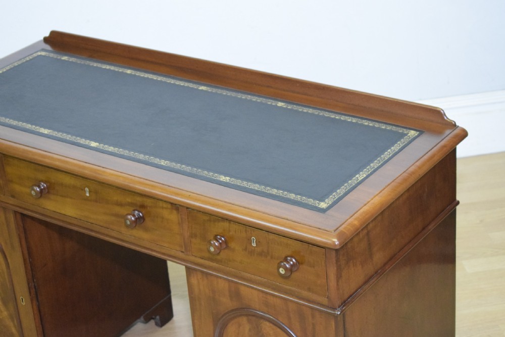 A Victorian mahogany pedestal desk featuring a dark green leather inset writing surface, three frieze drawers, and arched panel pedestal doors. View XIX
