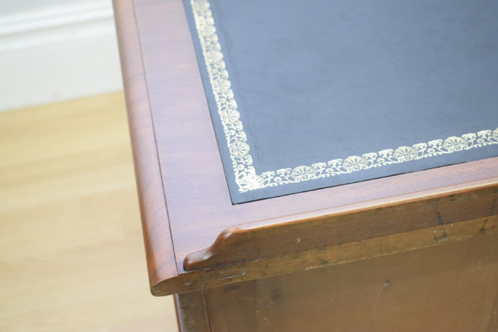 A Victorian mahogany pedestal desk featuring a dark green leather inset writing surface, three frieze drawers, and arched panel pedestal doors. View XXIII