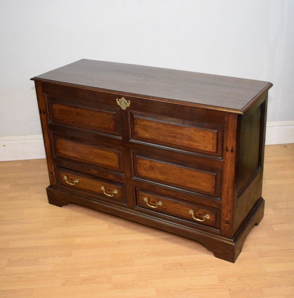 A Georgian dark oak Lancashire mule chest featuring a hinged top lid, panelled front sections with inlays, brass swan-neck handles, and bracket feet.